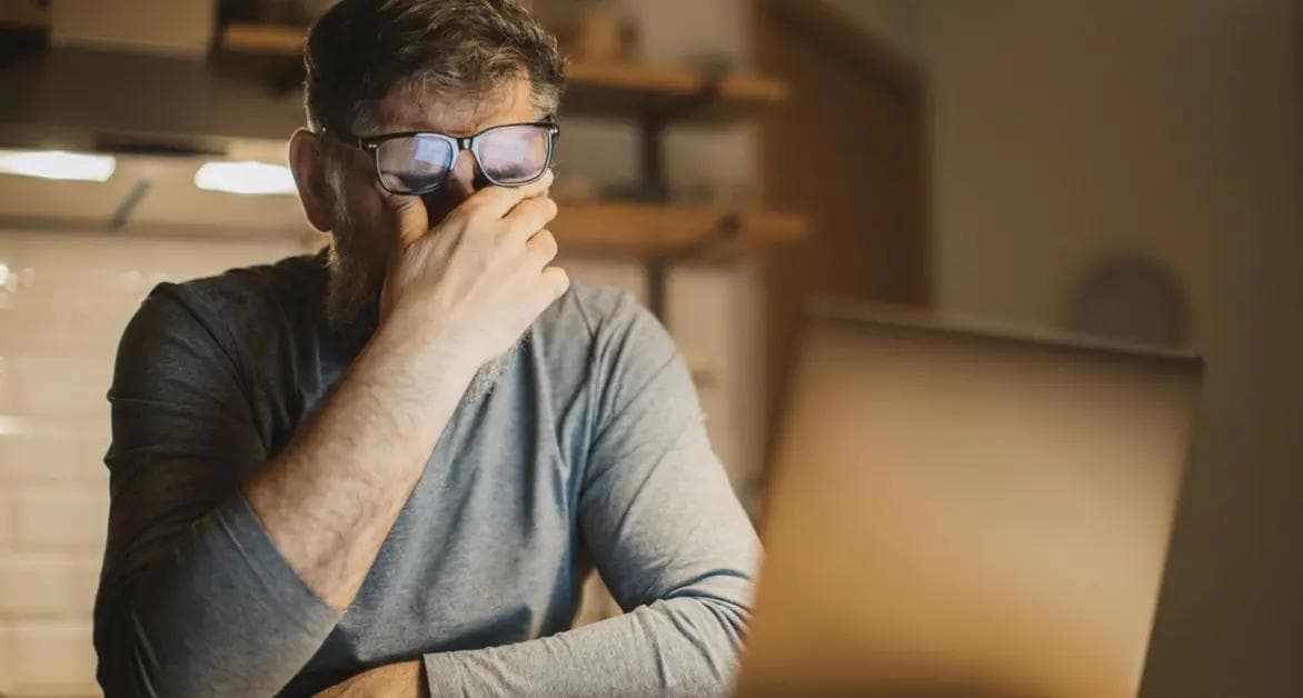 Træt mand i overgangsalderen gnider sig i øjnene foran en computer