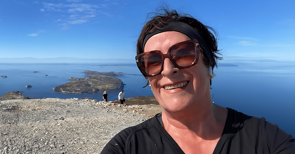 Kari (69) - smilende kvinde med kort, mørkt hår og solbriller