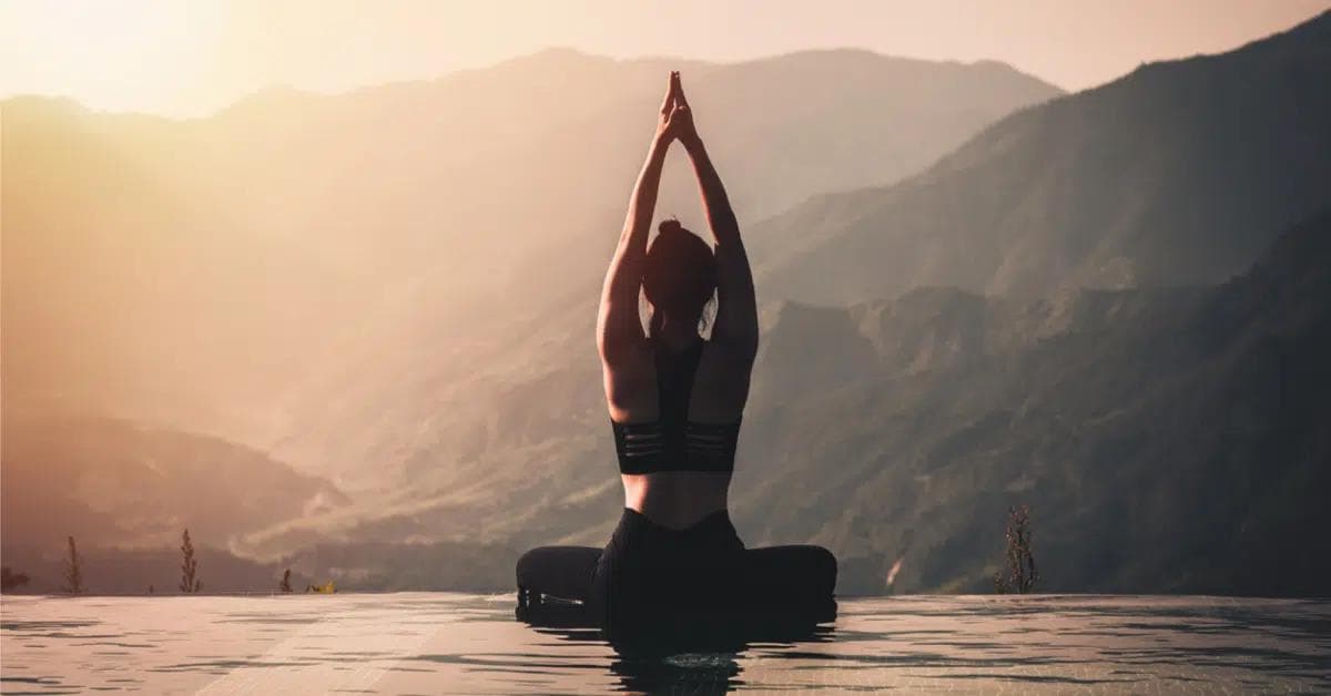 Kvinde i balancerende yogastilling med bjerge i baggrunden