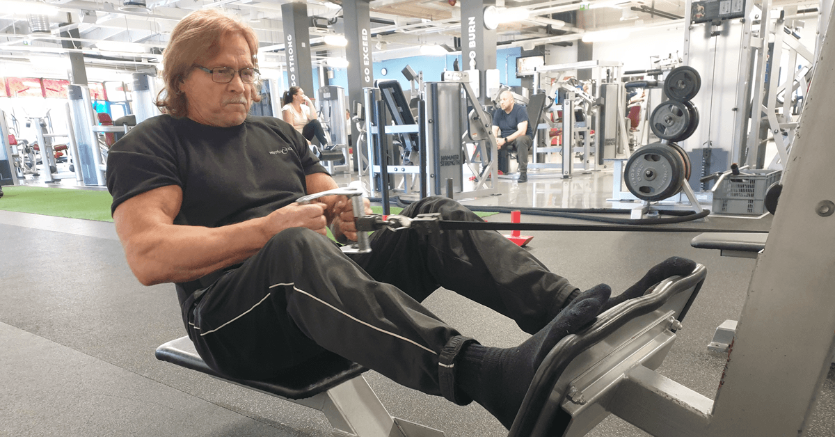 68-vuotias lihaksikas mies treenaamassa kuntosalilla voimaharjoittelua