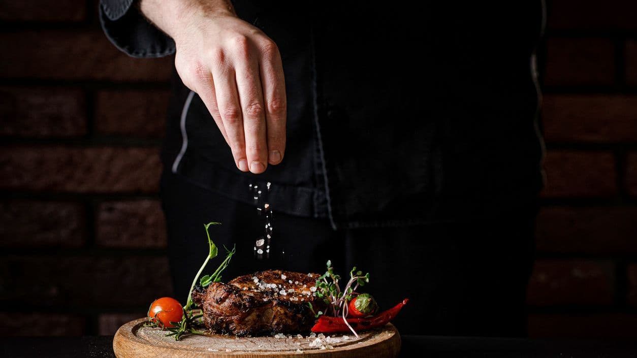 En mand som strøer slat på en steak inden servering