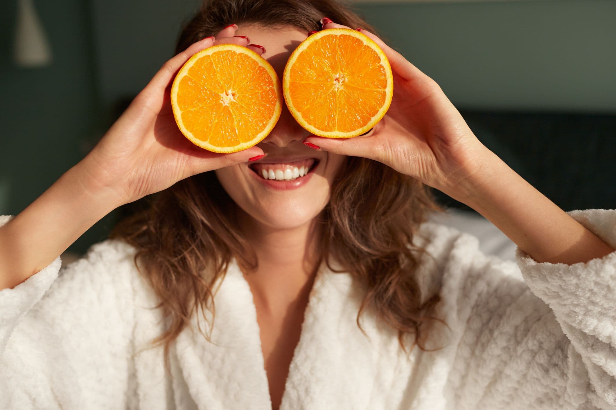 Onnellinen nainen, jolla on silmiensä edessä muutama C-vitamiinipitoinen appelsiini