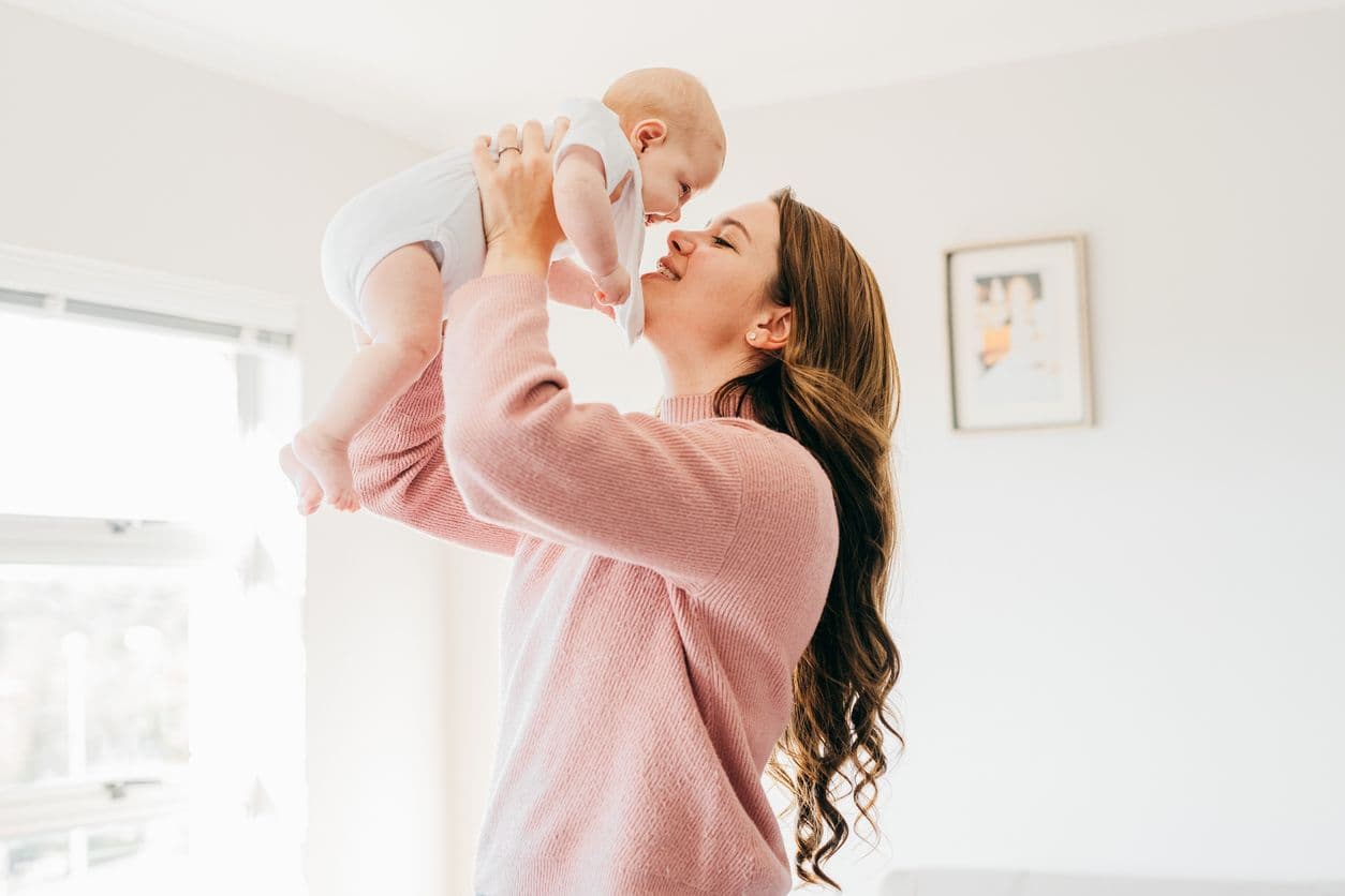 En mamma som håller upp sin bebis. Vitamin B2 är viktigt för ammande mödrar