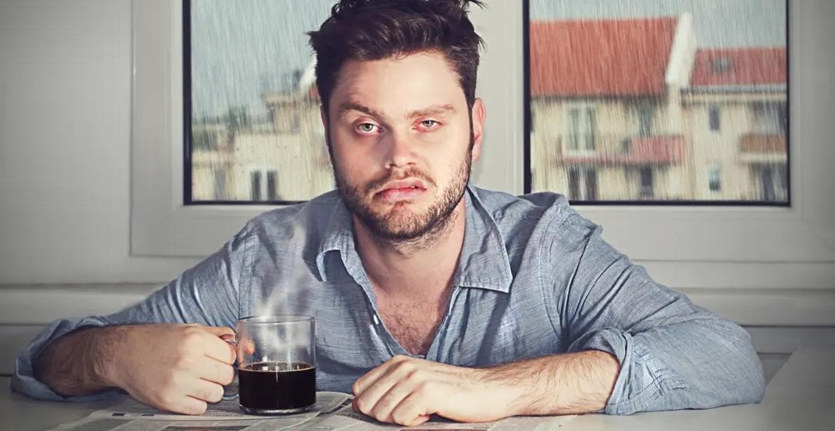 Trøtt mann som drikker kaffe og ser sur ut