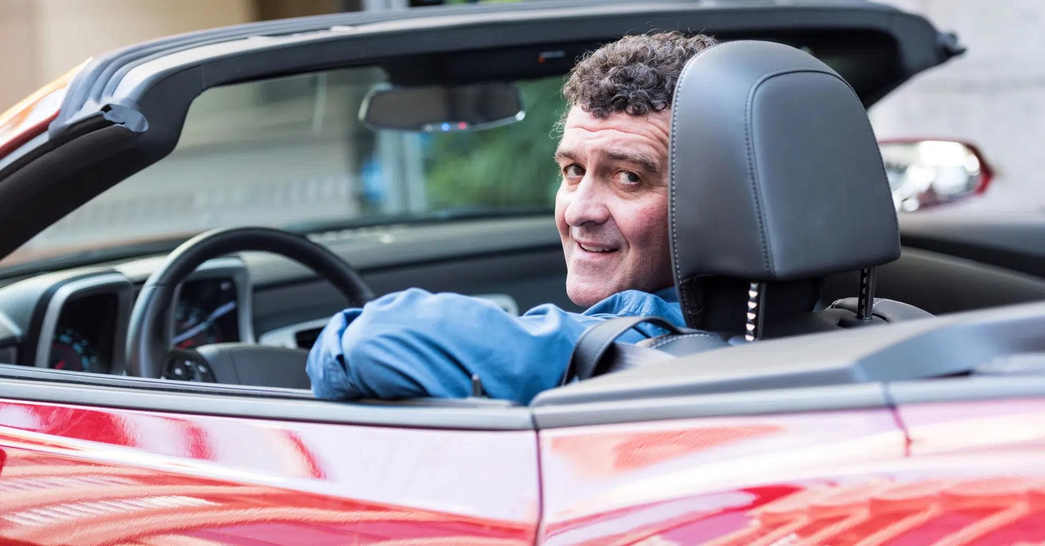 Medelålders man bakom ratten på en röd cabriolet